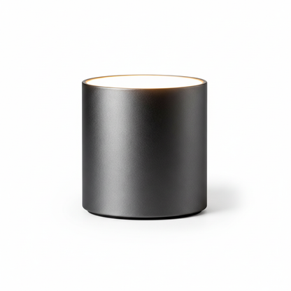 Noir Halo matte black cylindrical table lamp with a softly glowing top on a white background