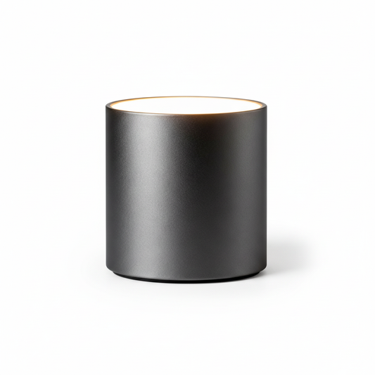 Noir Halo matte black cylindrical table lamp with a softly glowing top on a white background
